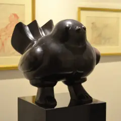 Een dikke, bronzen vogel, een typisch voorbeeld van de kunstwerken van Fernando Botero, staat op een sokkel. Op de achtergrond hangen schetsen.