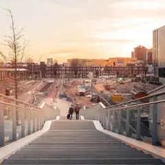 Twee mannen lopen een trap af in Utrecht, met op de achtergrond een bouwterrein en moderne gebouwen. Mooie foto locaties Utrecht.
