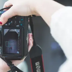 Hand met rode nagellak houdt een Canon m stand camera vast, focust op twee personen op het scherm.