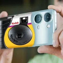 Een Kodak wegwerpcamera wordt vastgehouden naast een smartphone. Dit toont hoe werkt een wegwerpcamera: simpel en direct.