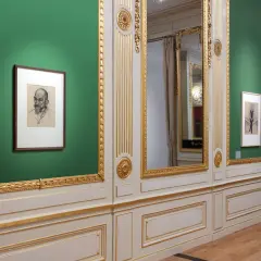 Een portret van Julie de Graag hangt aan een groene muur, naast een grote spiegel en een deur.