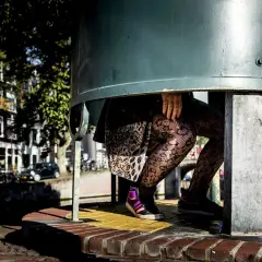 Een plassende vrouw in een urinoir, met opvallende panty's en sneakers.