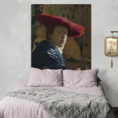 Een meisje met de rode hoed, geschilderd door Vermeer, kijkt mysterieus vanaf de muur boven een zachtroze bed.