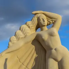 Zandstenen beeld van de Griekse godin Aphrodite, met golvend haar en een hand op haar hoofd, tegen een blauwe lucht met wolken.