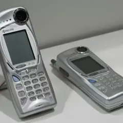 Twee zilverkleurige mobieltjes, waaronder de Kyocera VP-210, de eerste telefoon met camera.