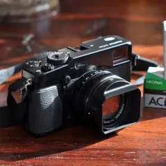 Zwarte Fujifilm X-E1 camera met lenskap en filmrolletjes Acros 100 op een houten tafel.
