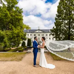 Bruidspaar geniet van hun fotoshoot kasteel. De bruid draagt een witte jurk met sluier, de bruidegom een blauw pak.