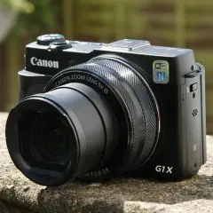 Zwarte Canon G1X Mark II camera met zoomlens, Wi-Fi en NFC, rustend op een stenen muur.