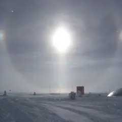 Een spectaculaire halo effect zon boven een besneeuwd landschap met gebouwen en vlaggen.