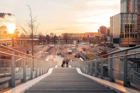 Twee mannen lopen een trap af in Utrecht, met op de achtergrond een bouwterrein en moderne gebouwen. Mooie foto locaties Utrecht.