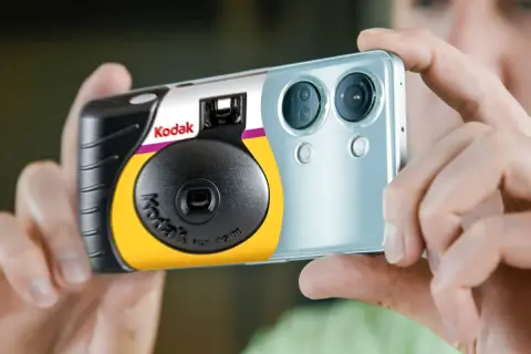 Een Kodak wegwerpcamera wordt vastgehouden naast een smartphone. Dit toont hoe werkt een wegwerpcamera: simpel en direct.