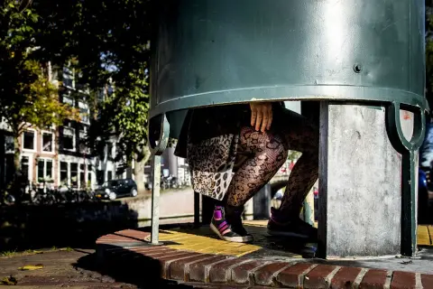 Een plassende vrouw in een urinoir, met opvallende panty's en sneakers.