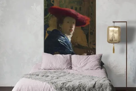 Een meisje met de rode hoed, geschilderd door Vermeer, kijkt mysterieus vanaf de muur boven een zachtroze bed.