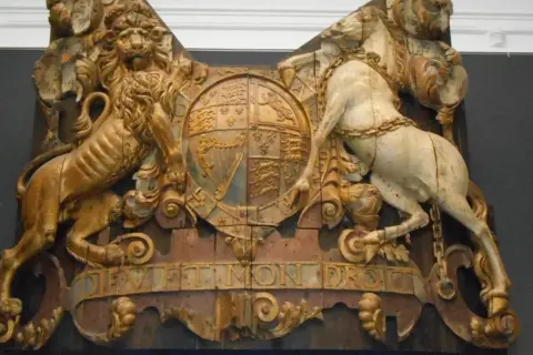 Gouden leeuw en wit paard houden een wapenschild vast, met de tekst "Dieu et mon droit". Een koninklijk pronkstuk, mogelijk van de spiegel Royal Charles.