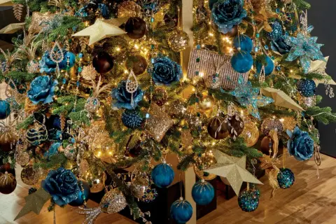 Een kerstboom vol met blauw goud, glinsterende ornamenten, blauwe bloemen en gouden sterren.