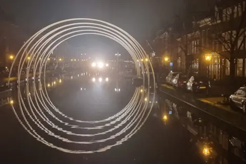 Een verlichte boog over een gracht in Leiden, met reflecties in het water. Dit is een prachtig staaltje kunst in Leiden.
