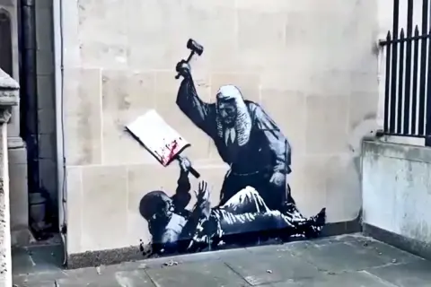 Kunstwerken van Banksy: een rechter slaat met een hamer op een boek, terwijl een figuur onderaan ligt.