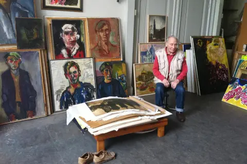 Jan Sierhuis, omringd door zijn kleurrijke portretten en stadsgezichten, in zijn atelier.