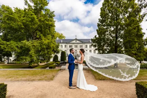 Bruidspaar geniet van hun fotoshoot kasteel. De bruid draagt een witte jurk met sluier, de bruidegom een blauw pak.