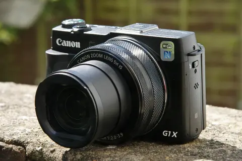 Zwarte Canon G1X Mark II camera met zoomlens, Wi-Fi en NFC, rustend op een stenen muur.