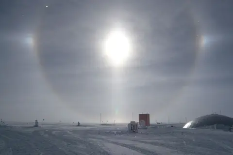 Een spectaculaire halo effect zon boven een besneeuwd landschap met gebouwen en vlaggen.