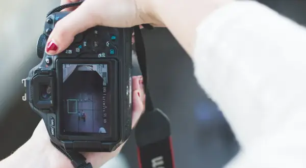 Hand met rode nagellak houdt een Canon m stand camera vast, focust op twee personen op het scherm.