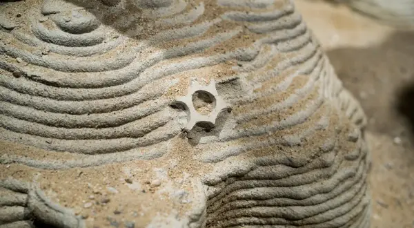 Gelaagde zand- en steenstructuren tonen prachtige patronen in de natuur, met een klein, stervormig object in het midden.