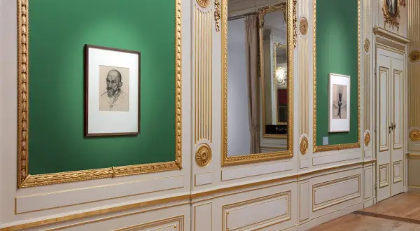 Een portret van Julie de Graag hangt aan een groene muur, naast een grote spiegel en een deur.