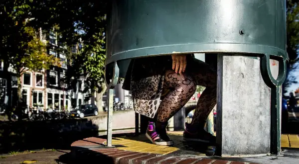 Een plassende vrouw in een urinoir, met opvallende panty's en sneakers.