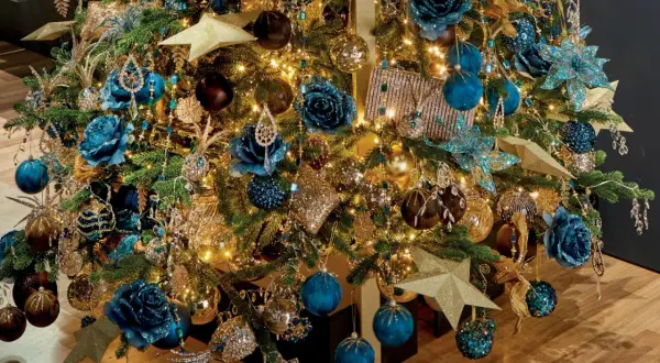 Een kerstboom vol met blauw goud, glinsterende ornamenten, blauwe bloemen en gouden sterren.