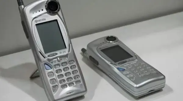 Twee zilverkleurige mobieltjes, waaronder de Kyocera VP-210, de eerste telefoon met camera.