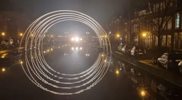 Een verlichte boog over een gracht in Leiden, met reflecties in het water. Dit is een prachtig staaltje kunst in Leiden.