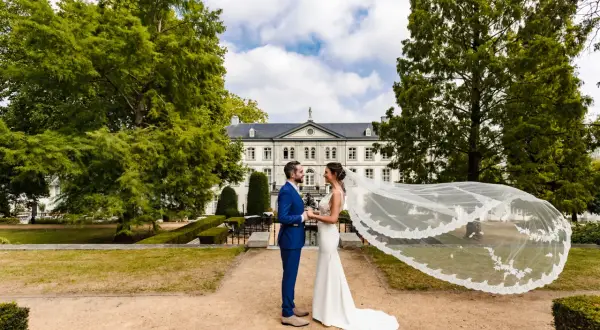 Bruidspaar geniet van hun fotoshoot kasteel. De bruid draagt een witte jurk met sluier, de bruidegom een blauw pak.