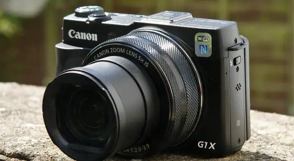 Zwarte Canon G1X Mark II camera met zoomlens, Wi-Fi en NFC, rustend op een stenen muur.