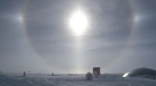 Een spectaculaire halo effect zon boven een besneeuwd landschap met gebouwen en vlaggen.