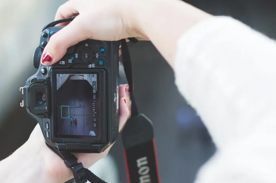 Hand met rode nagellak houdt een Canon m stand camera vast, focust op twee personen op het scherm.