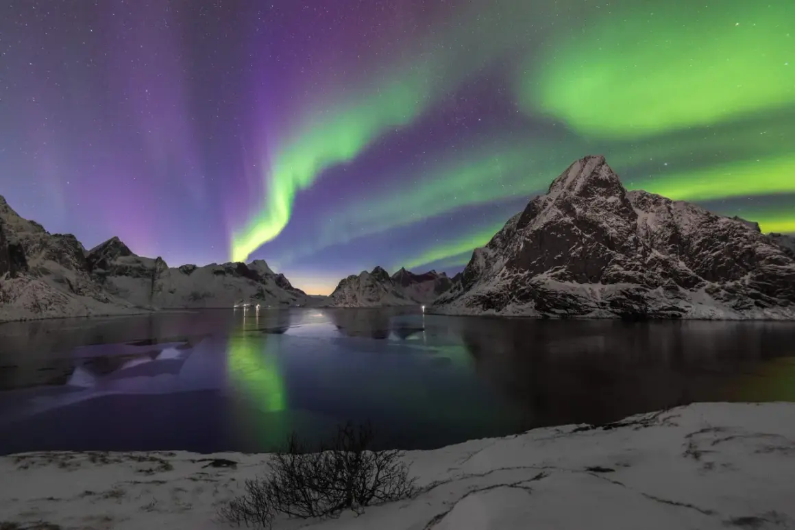 Spectaculaire foto's van het noorderlicht boven besneeuwde bergen en een bevroren meer. De groene en paarse gloed reflecteert in het water.