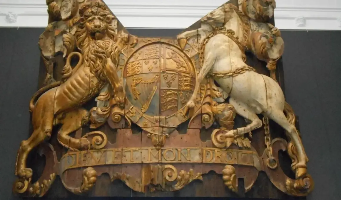 Gouden leeuw en wit paard houden een wapenschild vast, met de tekst "Dieu et mon droit". Een koninklijk pronkstuk, mogelijk van de spiegel Royal Charles.