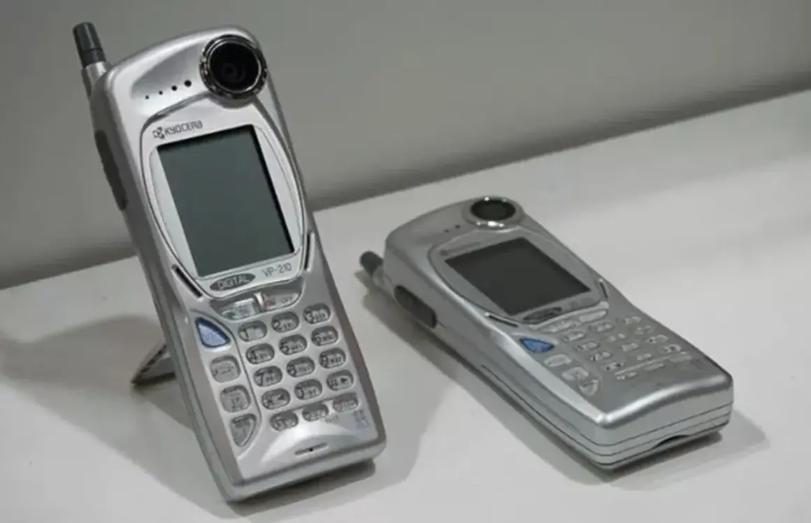 Twee zilverkleurige mobieltjes, waaronder de Kyocera VP-210, de eerste telefoon met camera.