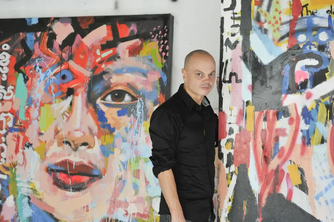 Peter Klashorst staat naast zijn kleurrijke, abstracte schilderijen. Een portret met een oog en rode lippen, en een ander werk met veel lijnen en verfspatten.