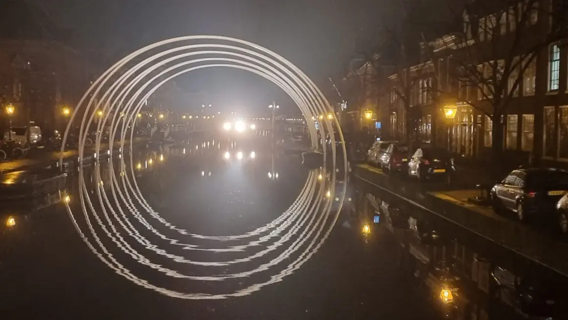Een verlichte boog over een gracht in Leiden, met reflecties in het water. Dit is een prachtig staaltje kunst in Leiden.