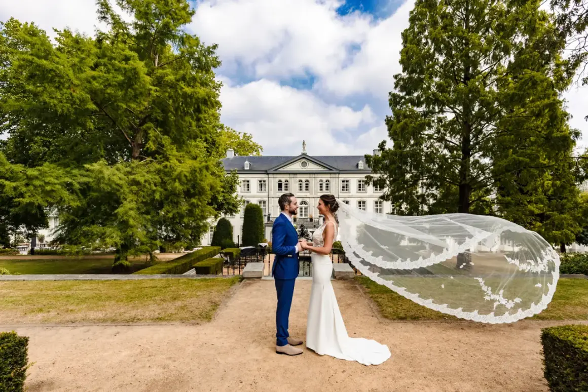 Bruidspaar geniet van hun fotoshoot kasteel. De bruid draagt een witte jurk met sluier, de bruidegom een blauw pak.