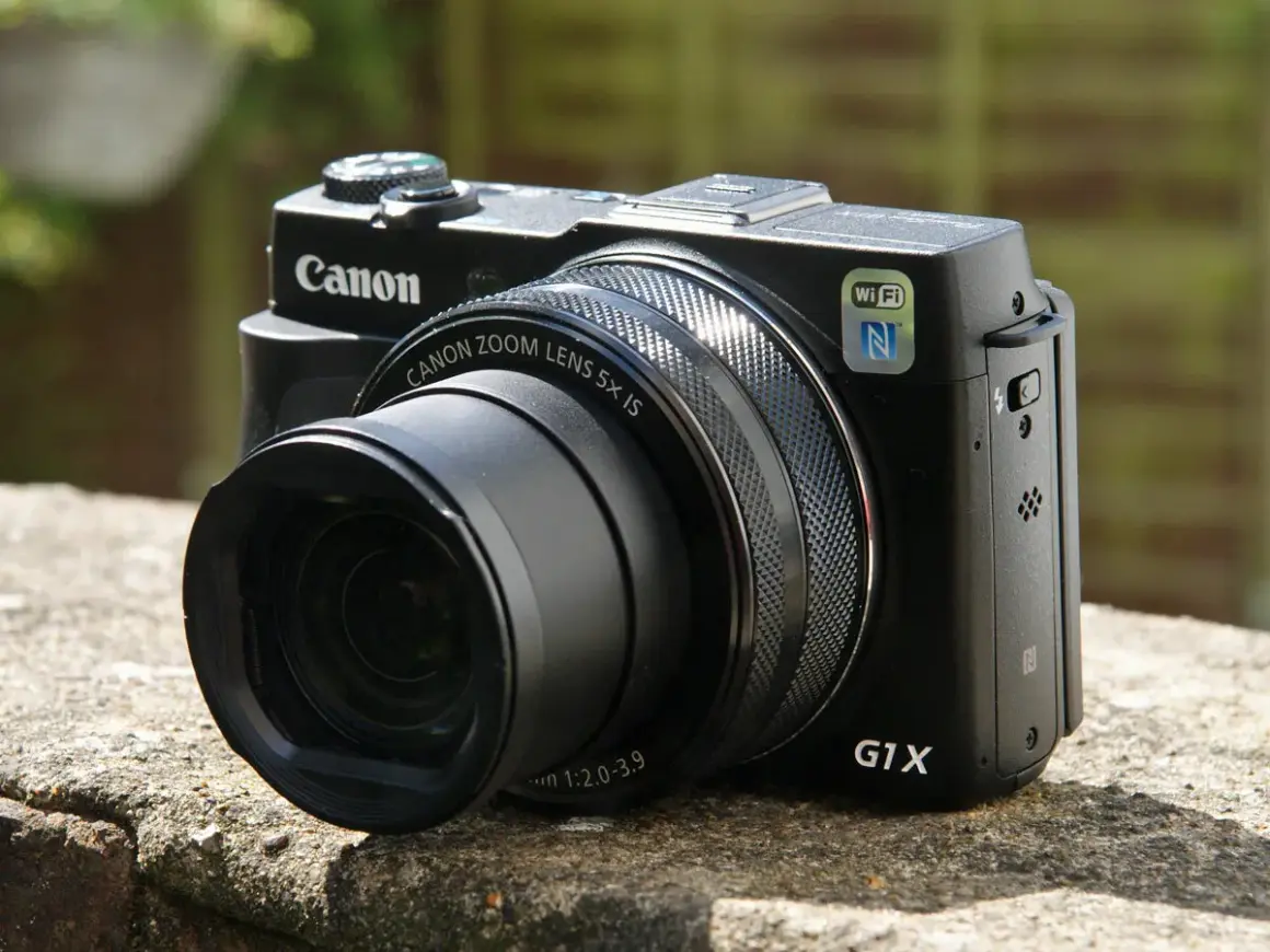 Zwarte Canon G1X Mark II camera met zoomlens, Wi-Fi en NFC, rustend op een stenen muur.