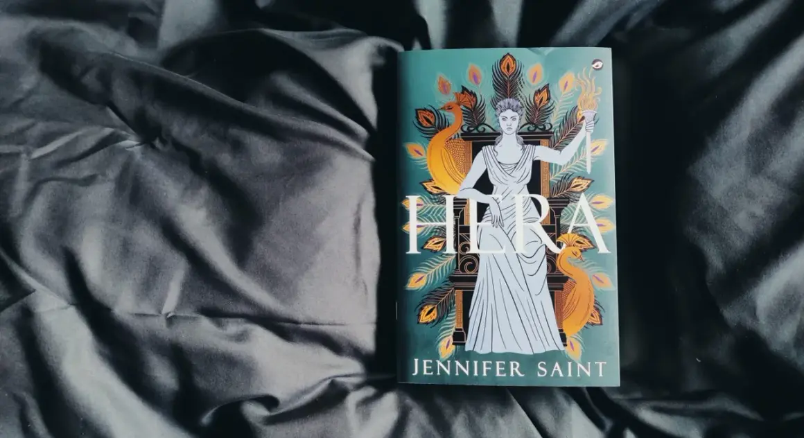 Boek "Hera" van Jennifer Saint, met de godin Hera afgebeeld met pauwenveren en een fakkel.