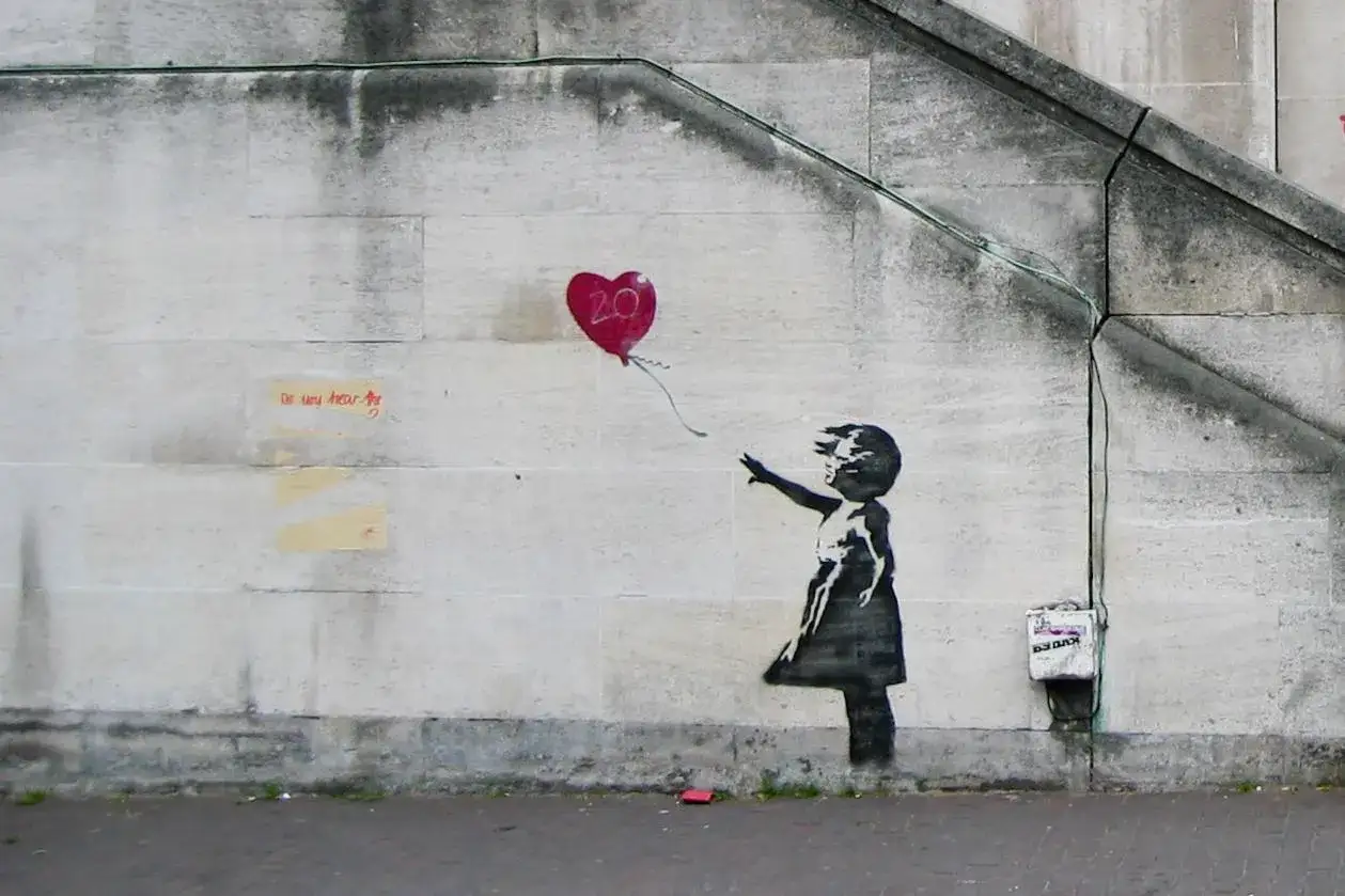 Een meisje reikt naar een rode ballon met het getal 20, een iconisch kunstwerk van Banksy.