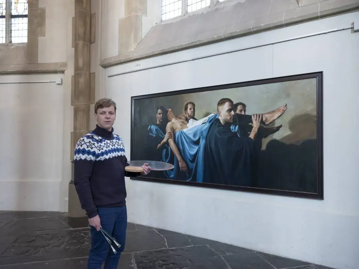 Een schilder staat naast zijn werk, een tafereel dat de zeven werken van barmhartigheid uitbeeldt, met mannen die een figuur dragen.