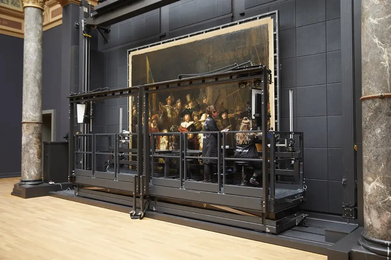 Restauratie Nachtwacht: twee conservatoren werken aan het beroemde schilderij op een verrijdbare werkplatform.