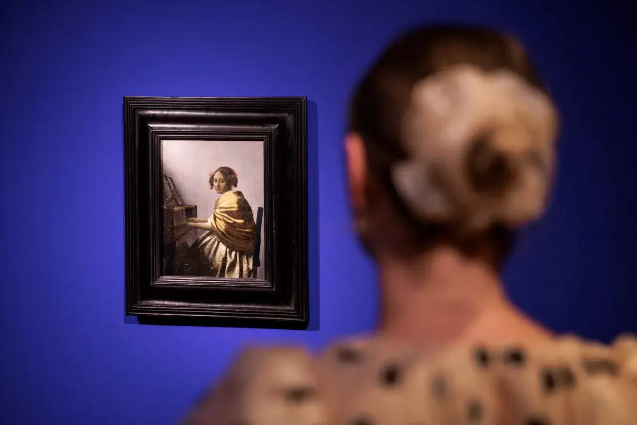 Een vrouw kijkt naar een schilderij van een dame aan een klavecimbel, een van de beroemde kunstwerken van Johannes Vermeer.