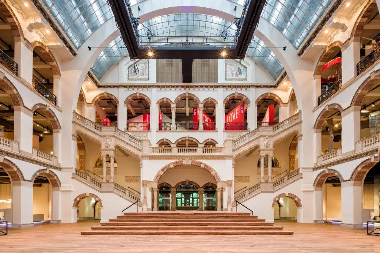 Indrukwekkende hal met trappen en balkons, versierd met rode banners met 'LOVE'. Een architectonisch meesterwerk, mogelijk ontworpen door Valika Smeulders.