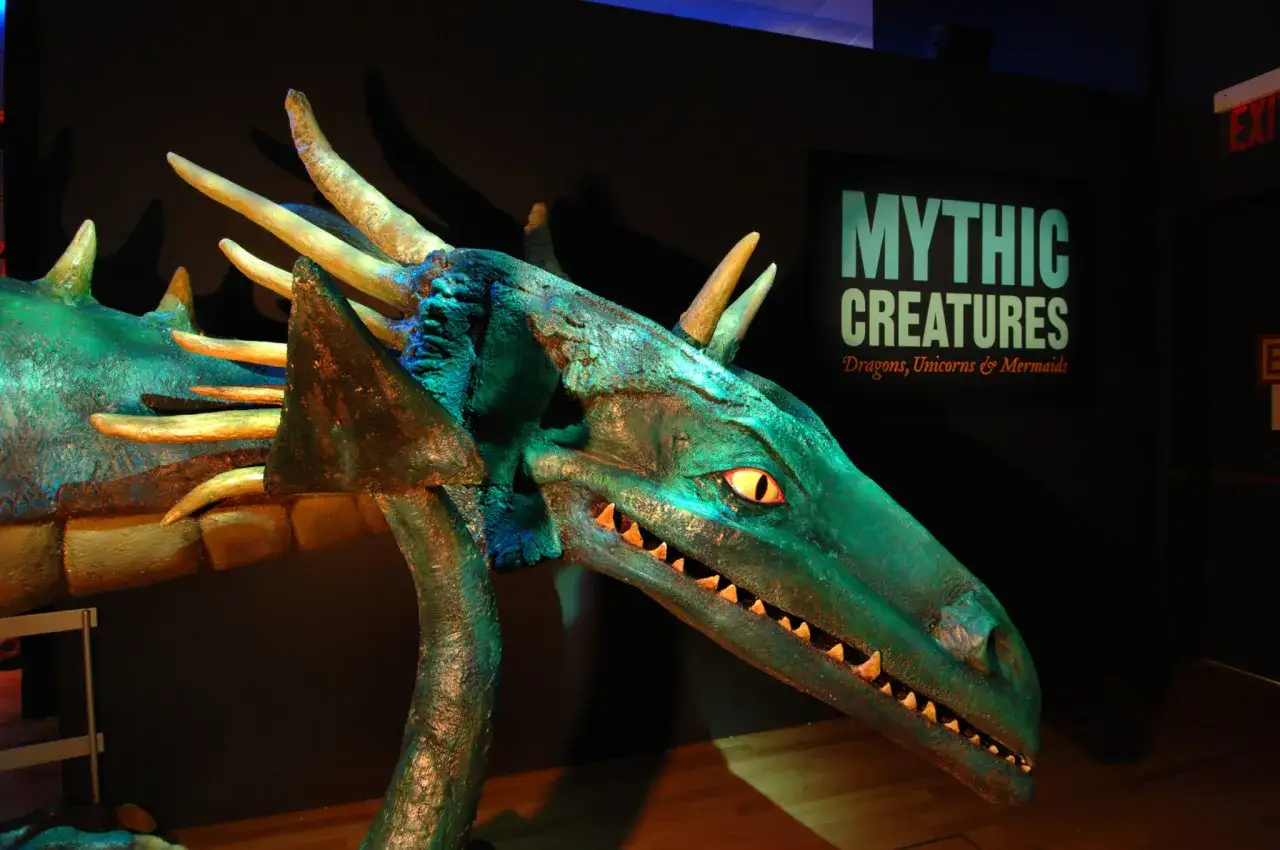 Een indrukwekkend groen fantasiewezen, een draak, met scherpe tanden en gele ogen, staat centraal in deze tentoonstelling over mythische wezens.